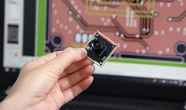 Camera module held in front of a PCB design workstation
